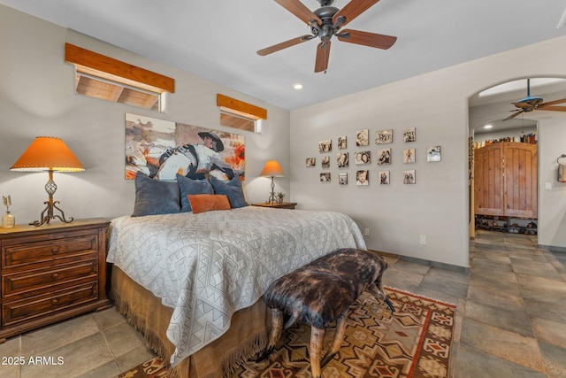 bedroom featuring stone finish flooring, arched walkways, baseboards, and ceiling fan