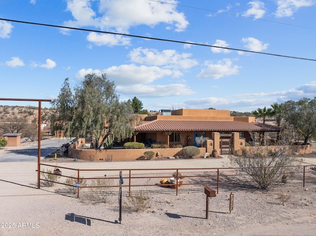 pueblo-style home featuring a tiled roof, a fenced front yard, and stucco siding