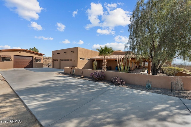 pueblo-style house featuring a garage, a fenced front yard, and stucco siding