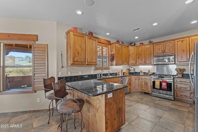 kitchen with visible vents, a peninsula, dark stone counters, a sink, and appliances with stainless steel finishes