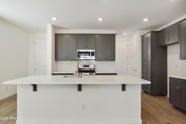 kitchen featuring stainless steel appliances, backsplash, a breakfast bar area, and wood finished floors