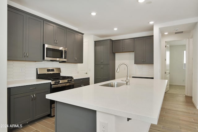 kitchen with appliances with stainless steel finishes, light countertops, a kitchen island with sink, and a sink