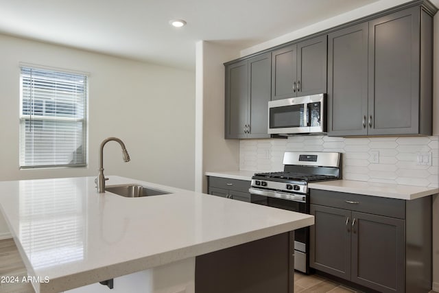 kitchen with appliances with stainless steel finishes, gray cabinets, a sink, and decorative backsplash