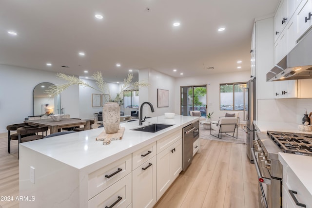 kitchen with high end appliances, sink, white cabinets, light hardwood / wood-style floors, and a large island