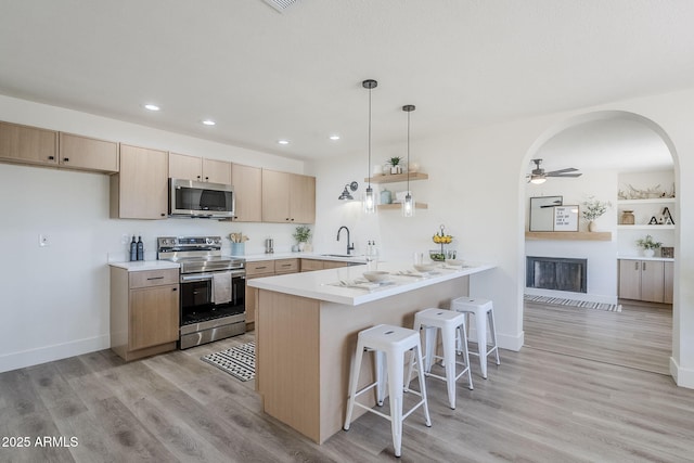 2337 E Contessa St, Mesa, AZ 85213 - kitchen featuring appliances with stainless steel finishes, a peninsula, a breakfast bar, a large fireplace, and light wood-style floors