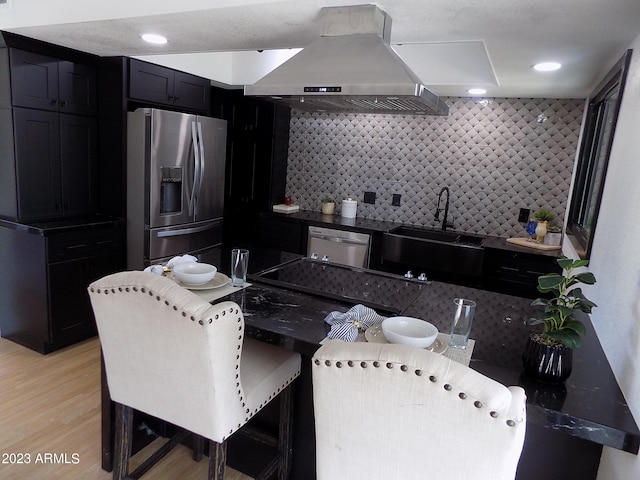 kitchen featuring backsplash, light hardwood / wood-style floors, sink, stainless steel appliances, and wall chimney range hood