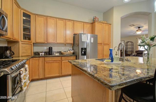 14298 W Amelia Ave, Goodyear, AZ 85395 - kitchen with appliances with stainless steel finishes, arched walkways, light tile patterned floors, a sink, and dark stone countertops