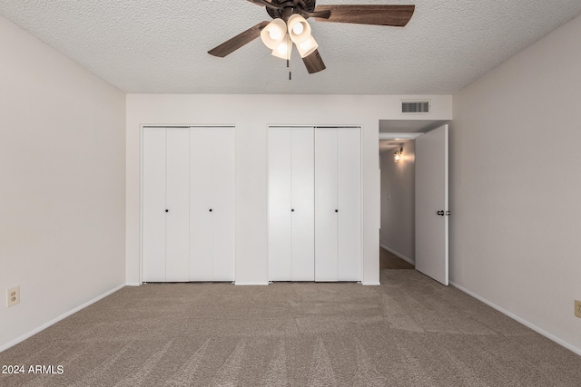 unfurnished bedroom featuring a textured ceiling, two closets, carpet flooring, and ceiling fan