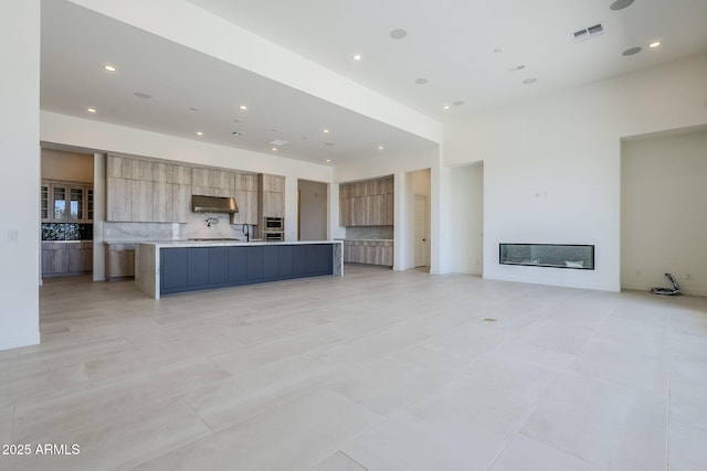 kitchen with light tile patterned flooring, a large island, sink, and backsplash