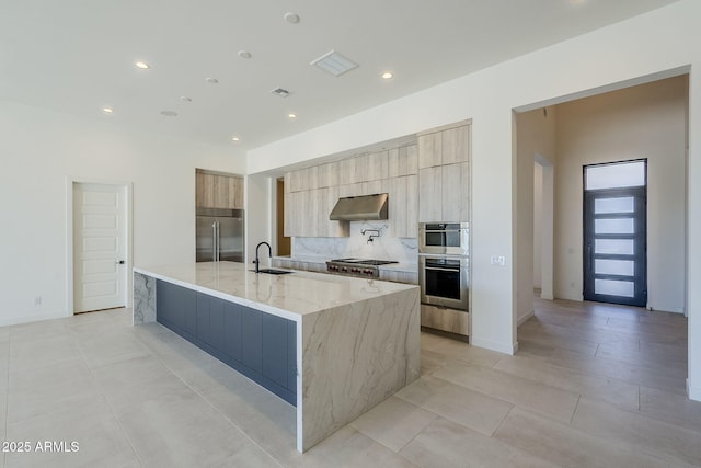 kitchen with sink, backsplash, stainless steel appliances, a spacious island, and light stone counters