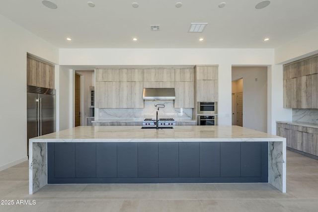 kitchen featuring built in fridge, light brown cabinetry, decorative backsplash, light stone counters, and a spacious island