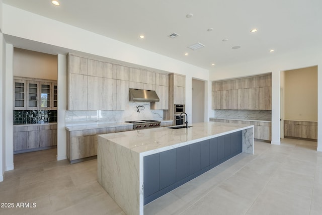 kitchen with a large island, sink, tasteful backsplash, light stone countertops, and stainless steel gas cooktop