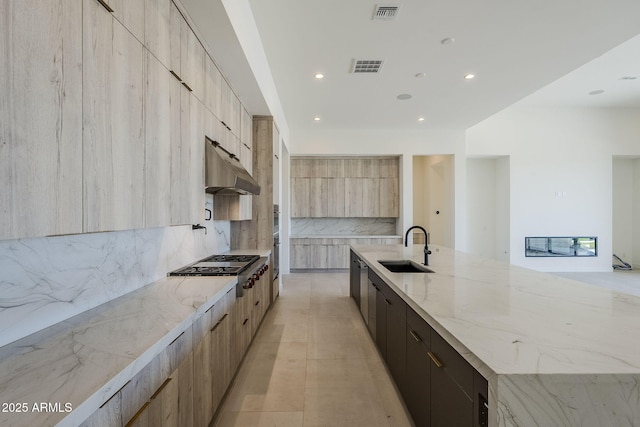 kitchen featuring stainless steel gas stovetop, sink, decorative backsplash, light stone countertops, and a spacious island