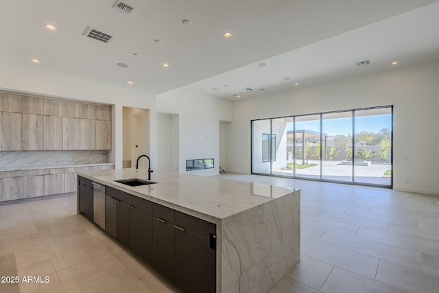 kitchen with tasteful backsplash, dishwasher, sink, a large island with sink, and light stone countertops