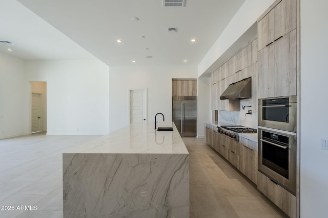 kitchen with sink, light stone counters, tasteful backsplash, a large island with sink, and appliances with stainless steel finishes