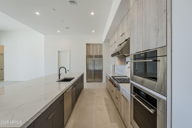 kitchen featuring light stone countertops, appliances with stainless steel finishes, sink, and light brown cabinetry