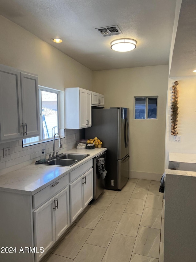 kitchen with light tile patterned flooring, white cabinetry, dishwasher, sink, and decorative backsplash