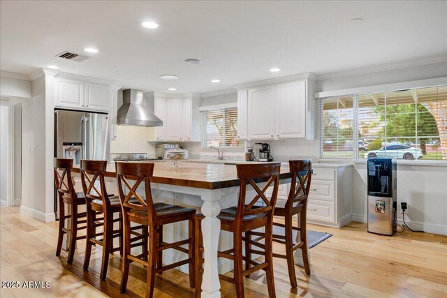 1831 E Rovey Ave, Phoenix, AZ 85016 - kitchen featuring stainless steel fridge with ice dispenser, wall chimney exhaust hood, crown molding, butcher block countertops, and white cabinets