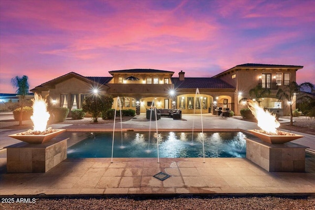 pool at dusk with a patio area, pool water feature, and an outdoor fire pit