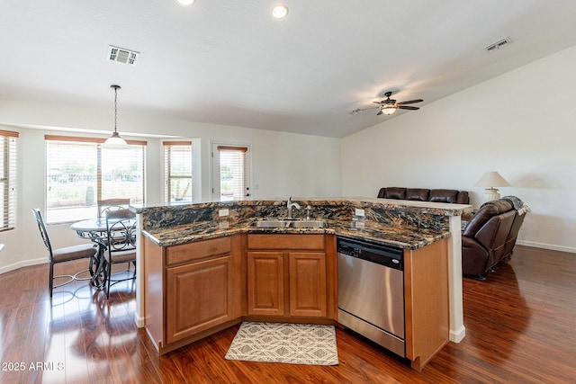 kitchen featuring sink, decorative light fixtures, dark stone countertops, stainless steel dishwasher, and an island with sink