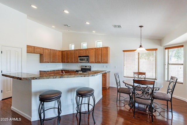 kitchen with dark wood-type flooring, stainless steel appliances, decorative light fixtures, and a kitchen island