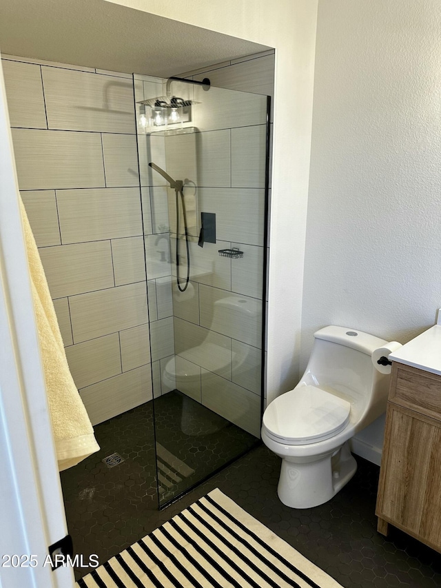 bathroom featuring toilet, vanity, tiled shower, and tile patterned floors