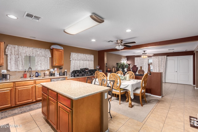 kitchen with light tile patterned floors, ceiling fan, stainless steel dishwasher, sink, and a center island