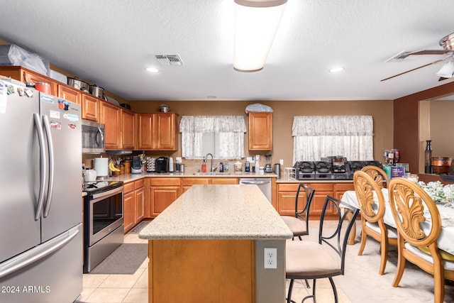 kitchen featuring ceiling fan, a kitchen island, a textured ceiling, sink, and stainless steel appliances