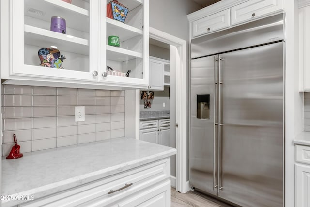 kitchen featuring light stone counters, tasteful backsplash, white cabinets, and built in refrigerator