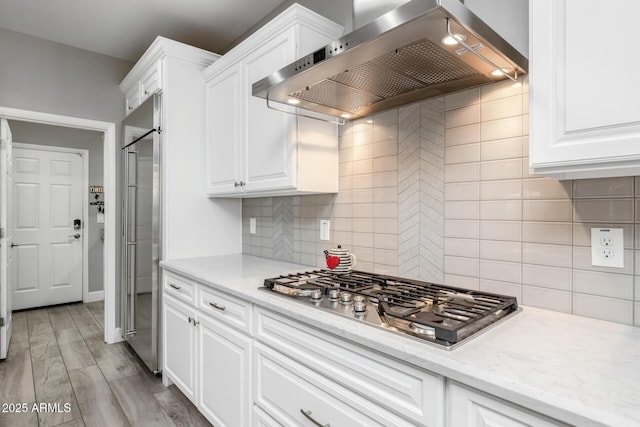 kitchen featuring white cabinetry, appliances with stainless steel finishes, light hardwood / wood-style flooring, and wall chimney range hood