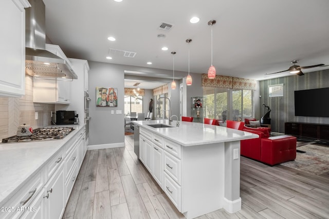 kitchen featuring pendant lighting, a kitchen island with sink, extractor fan, stainless steel gas cooktop, and white cabinets