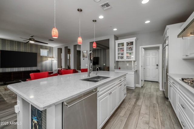 kitchen with stainless steel appliances, an island with sink, white cabinetry, and decorative light fixtures