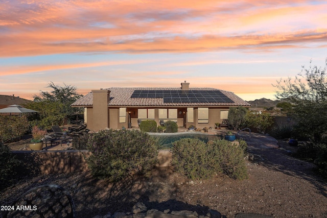 back house at dusk featuring solar panels and a patio area