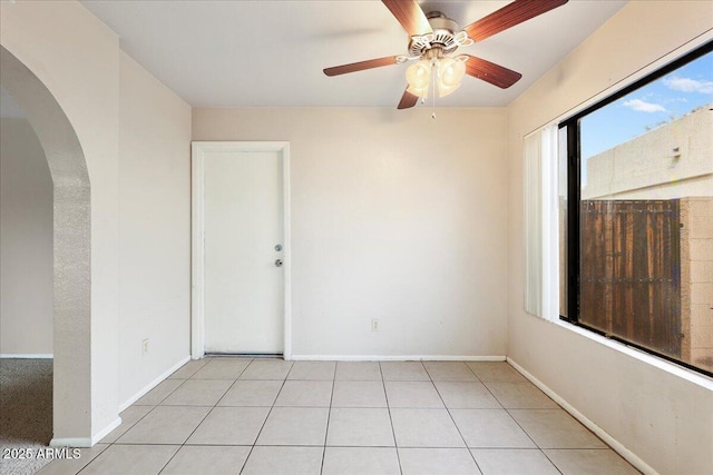 unfurnished room featuring arched walkways, baseboards, and a ceiling fan