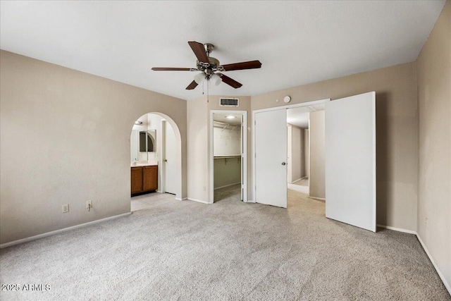 unfurnished bedroom featuring arched walkways, visible vents, light colored carpet, and baseboards