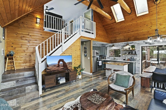 living room featuring wood ceiling, a skylight, ceiling fan, wooden walls, and high vaulted ceiling