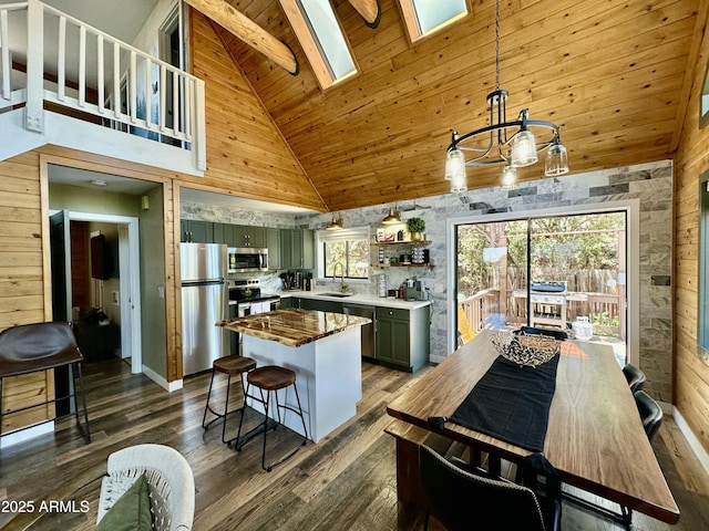 kitchen with wooden ceiling, appliances with stainless steel finishes, a skylight, high vaulted ceiling, and decorative light fixtures