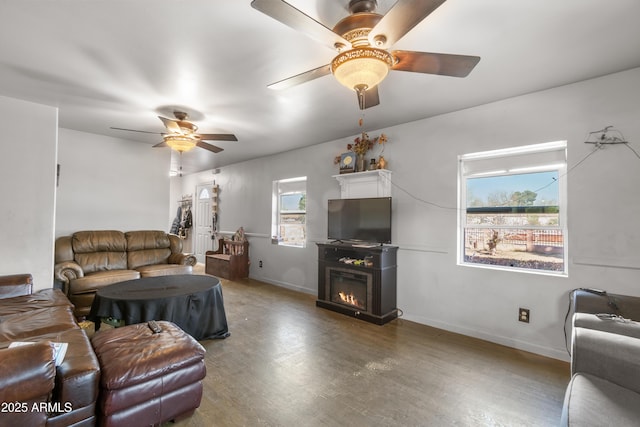 living area with a glass covered fireplace, wood finished floors, baseboards, and a ceiling fan