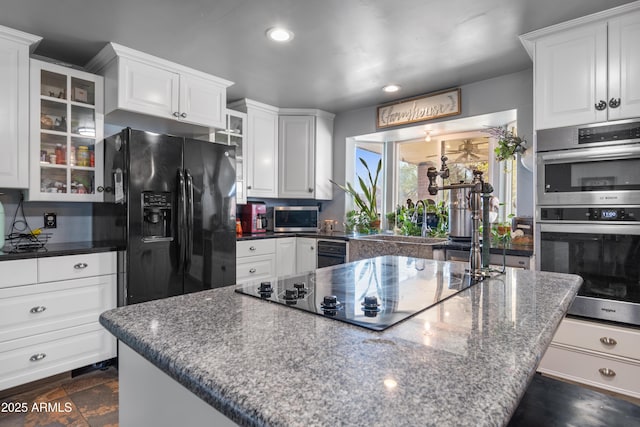 kitchen featuring glass insert cabinets, black appliances, a center island, and white cabinetry