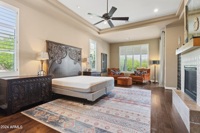 bedroom featuring multiple windows, a fireplace, dark hardwood / wood-style floors, and ceiling fan