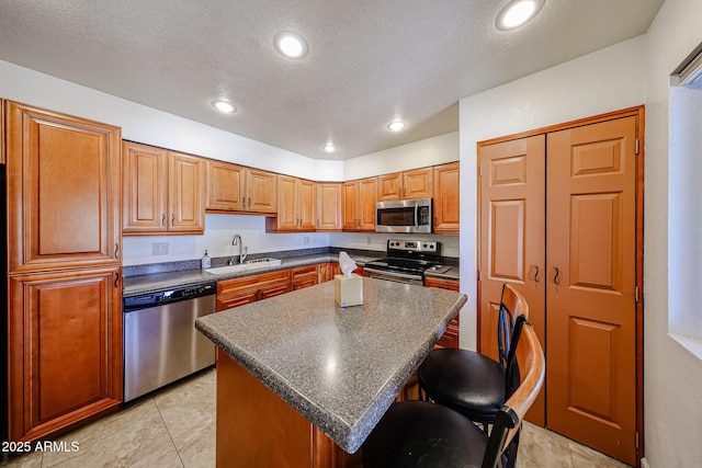 kitchen with sink, a center island, a textured ceiling, a kitchen breakfast bar, and stainless steel appliances