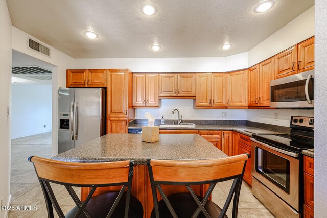 kitchen with sink, a breakfast bar area, light tile patterned floors, stainless steel appliances, and a textured ceiling