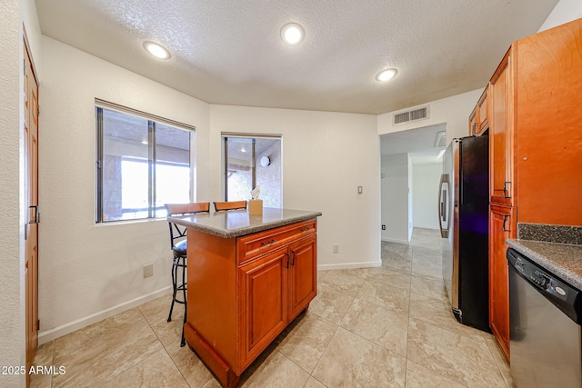 kitchen with stainless steel appliances, a center island, a textured ceiling, and a kitchen breakfast bar