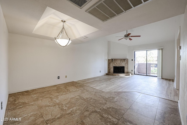 unfurnished living room featuring light tile patterned floors, a tray ceiling, a fireplace, and ceiling fan