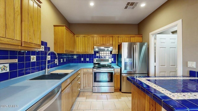 kitchen with stainless steel appliances, sink, tile countertops, light tile patterned floors, and decorative backsplash