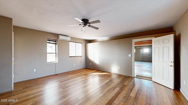 spare room featuring light wood-type flooring, ceiling fan, and an AC wall unit