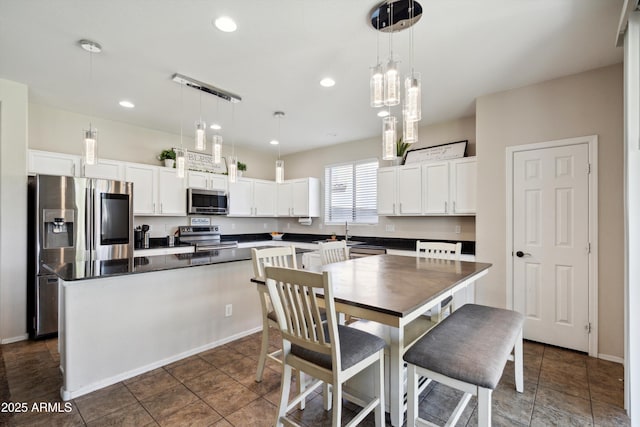 kitchen featuring pendant lighting, white cabinets, a kitchen island, appliances with stainless steel finishes, and dark countertops