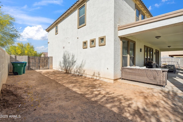 view of home's exterior featuring outdoor lounge area, stucco siding, a patio area, a fenced backyard, and a gate