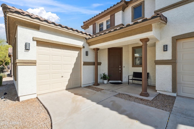 view of front of home featuring an attached garage, a tiled roof, concrete driveway, and stucco siding