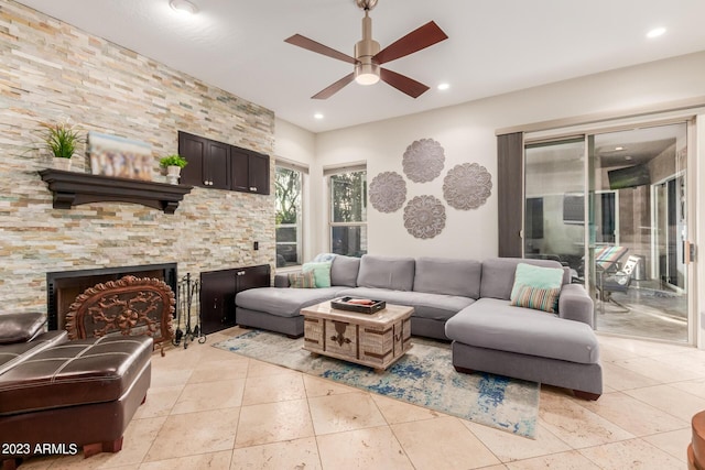 tiled living room featuring a stone fireplace and ceiling fan